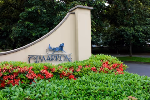 Entrance sign with a horse emblem and surrounding red and green shrubbery.