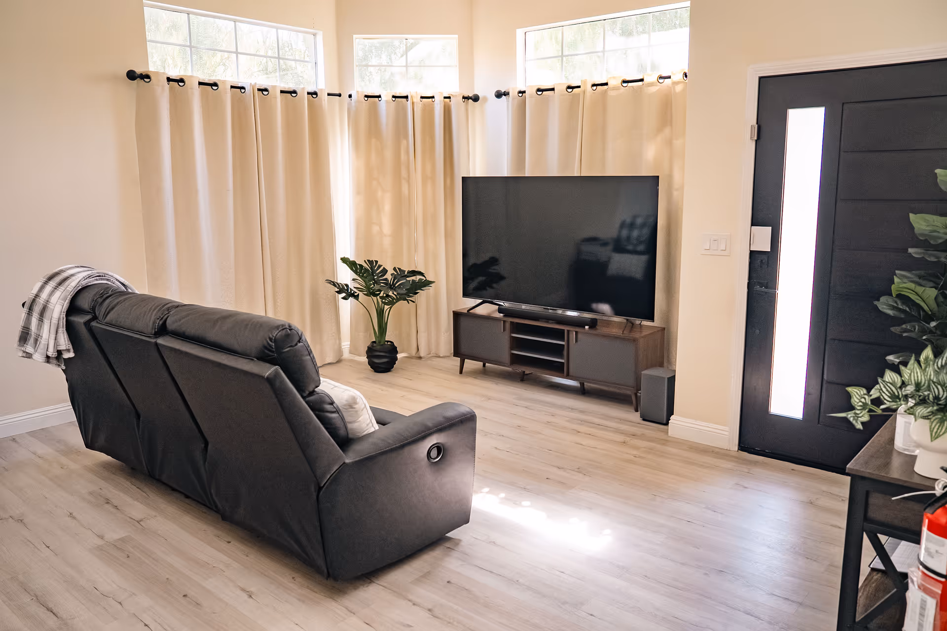 A bright living room with a reclining sofa, large TV, and neutral decor.