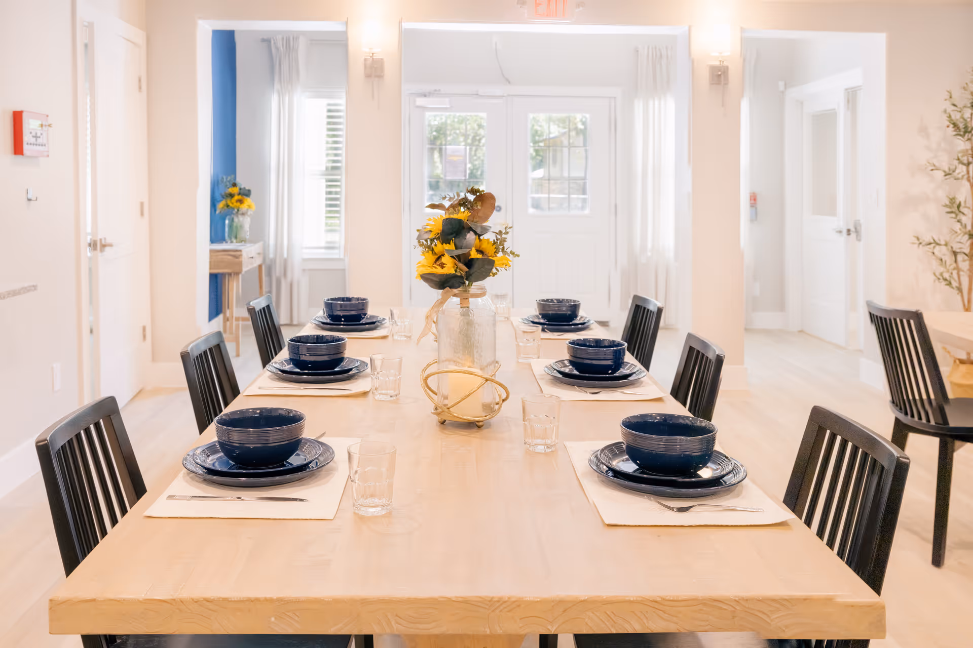 A bright dining room with a long table set with blue bowls and a centerpiece.