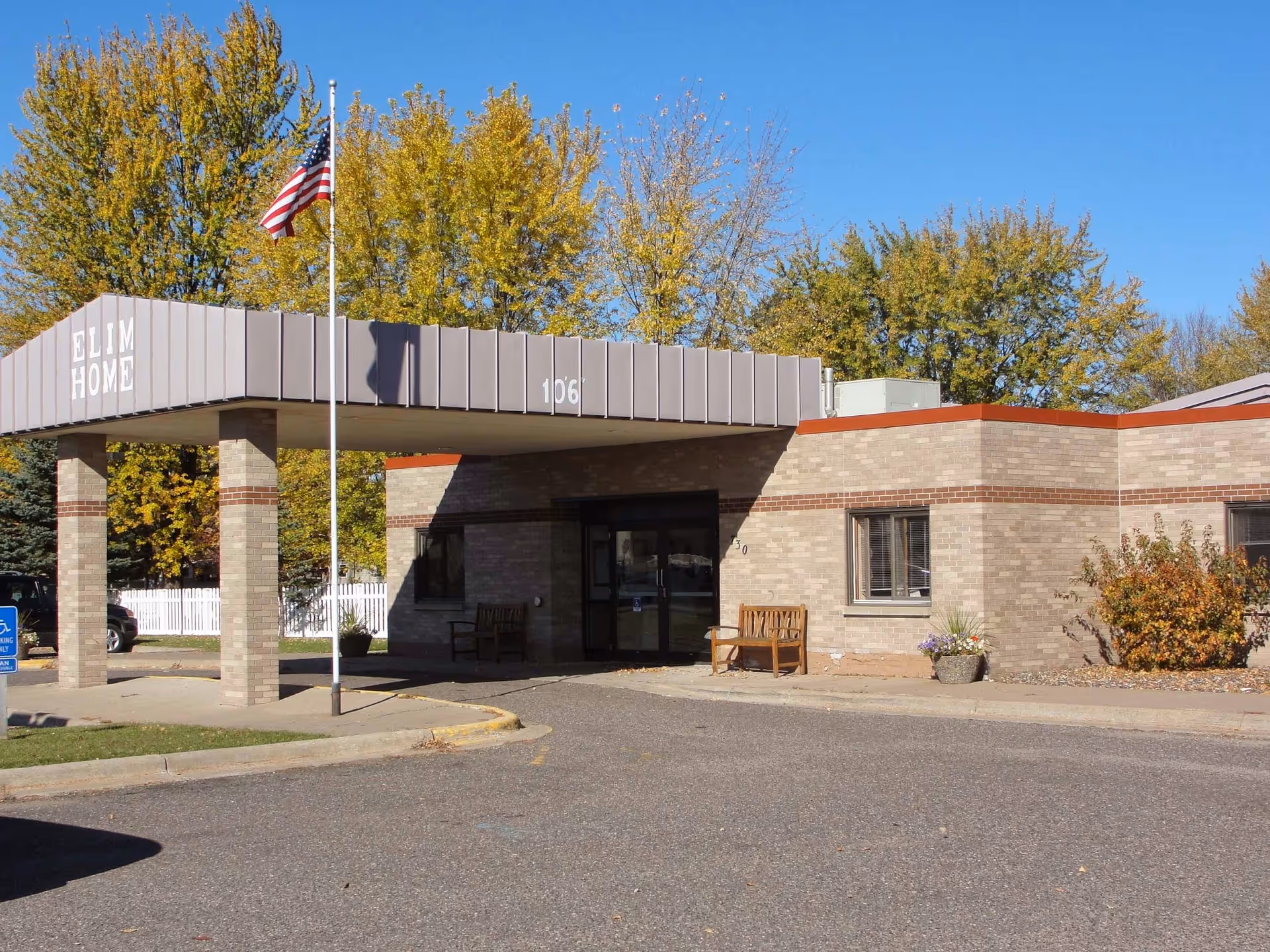 Elim Home Milaca entrance with flagpole and autumn-colored trees.