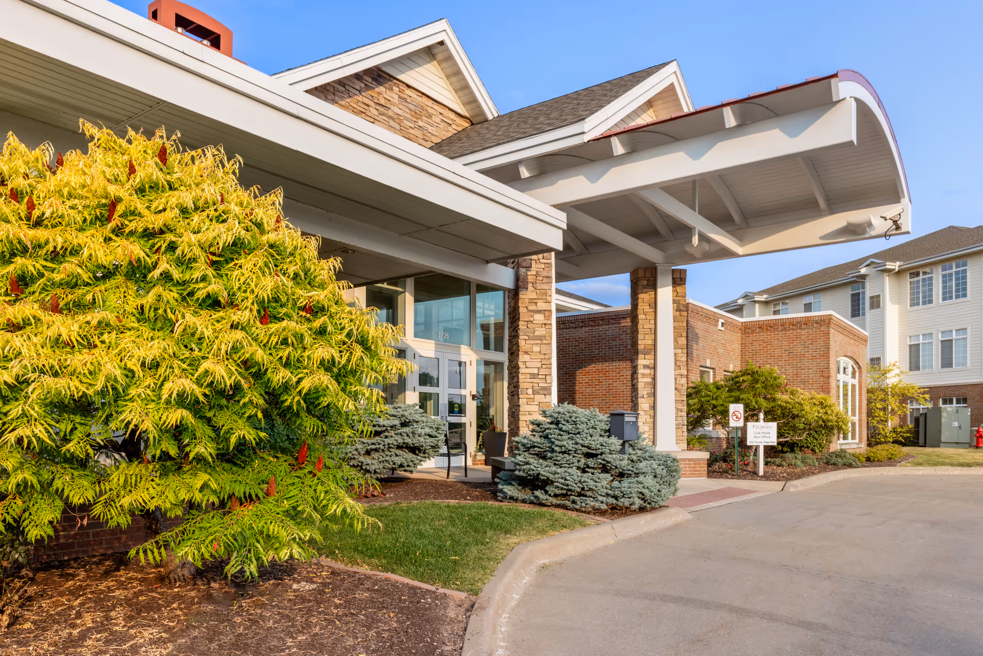 Entrance of The Fountains senior living facility with brick facade and landscaped shrubs