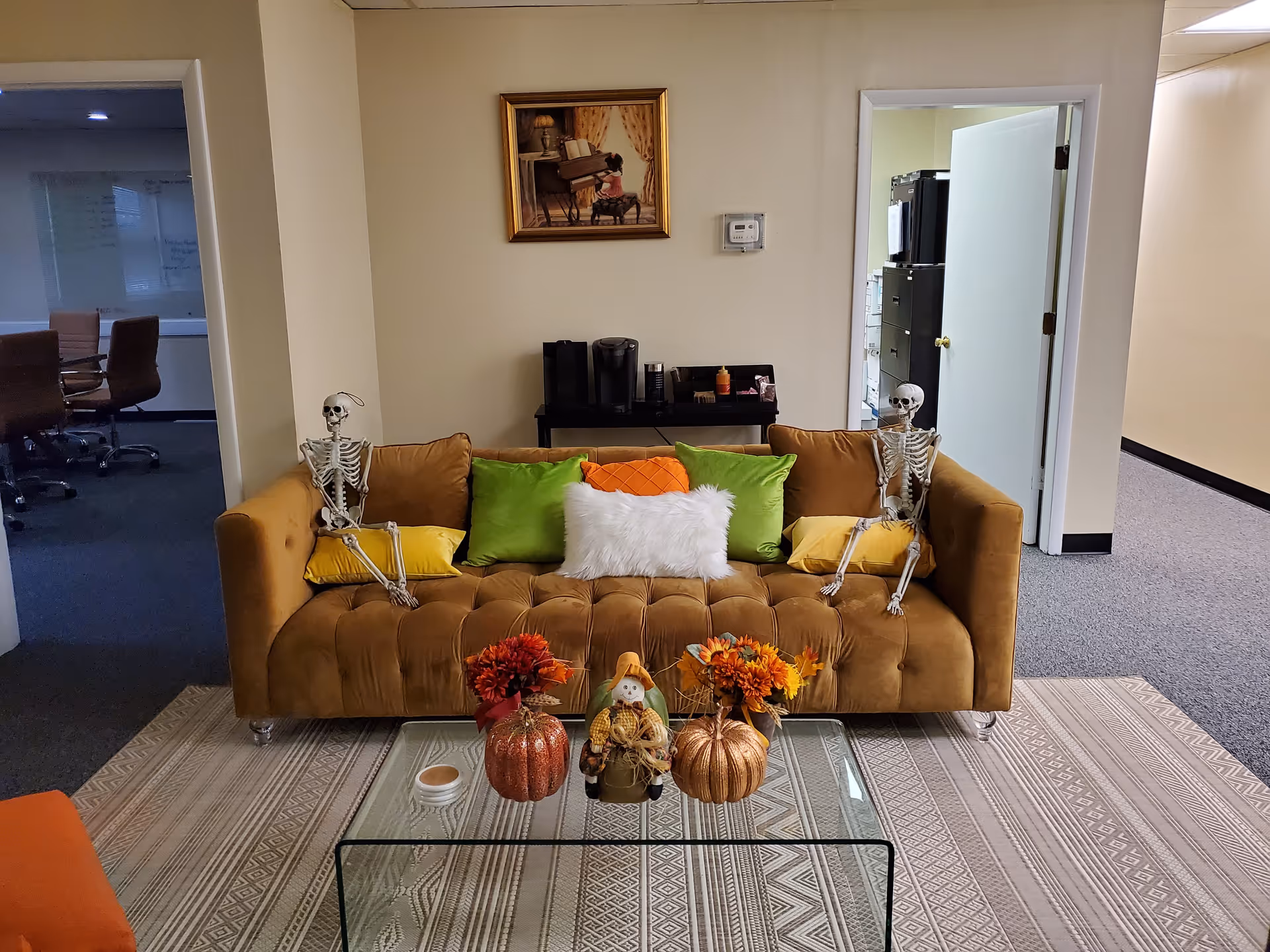 Cozy lounge with a brown tufted sofa, skeleton decorations, fall decor, and a glass coffee table.