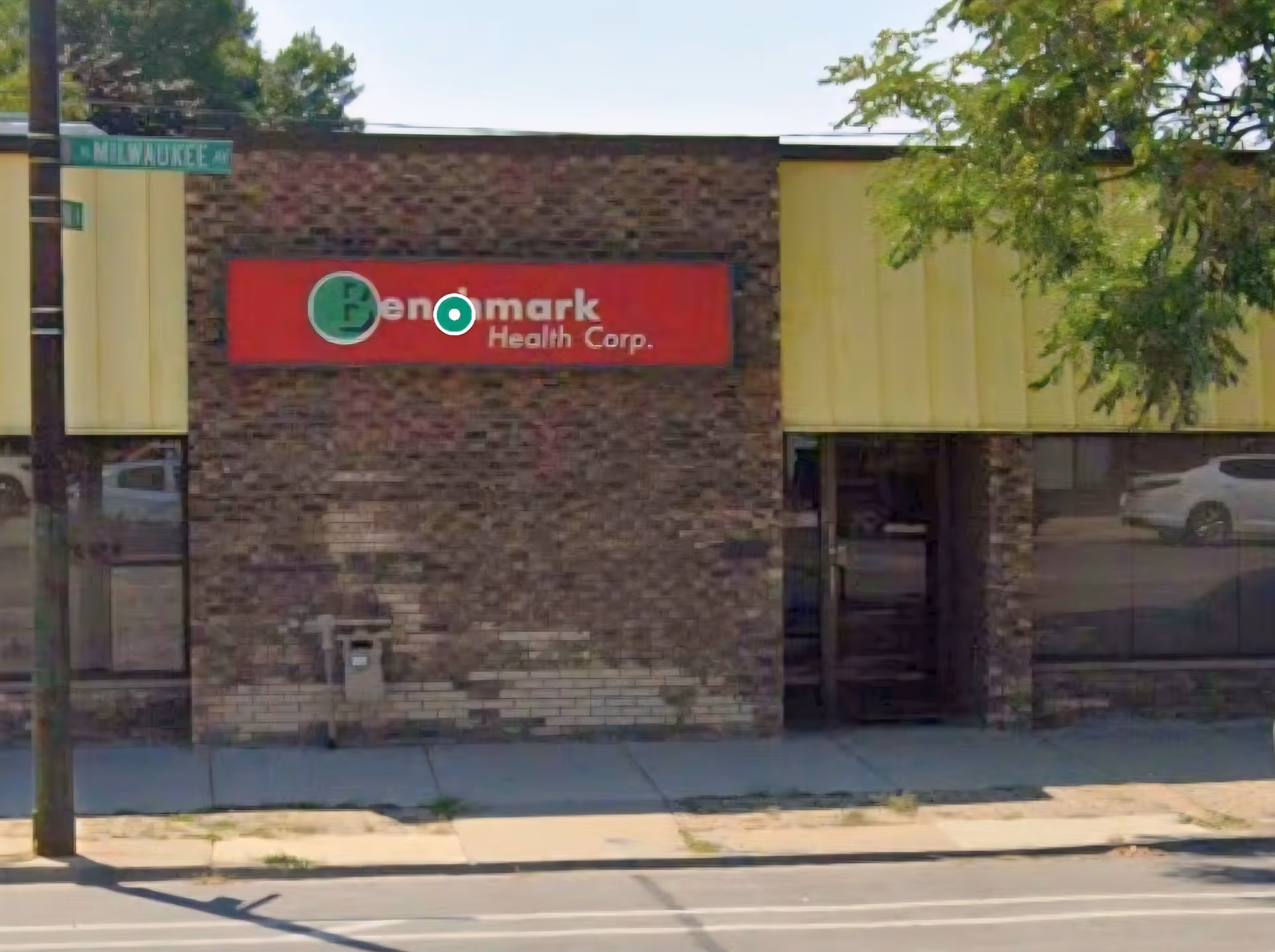 Brick storefront with Benchmark Health Corp sign and yellow facade along sidewalk.