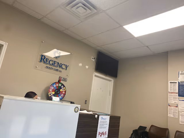 Reception desk in Regency Health Care lobby with sign, wheel, and TV.