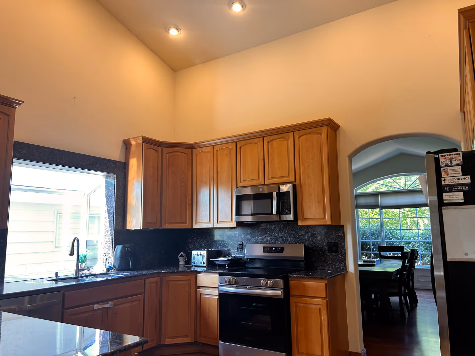 Bright kitchen with wooden cabinets, black granite countertops, stainless appliances, and adjacent dining area.
