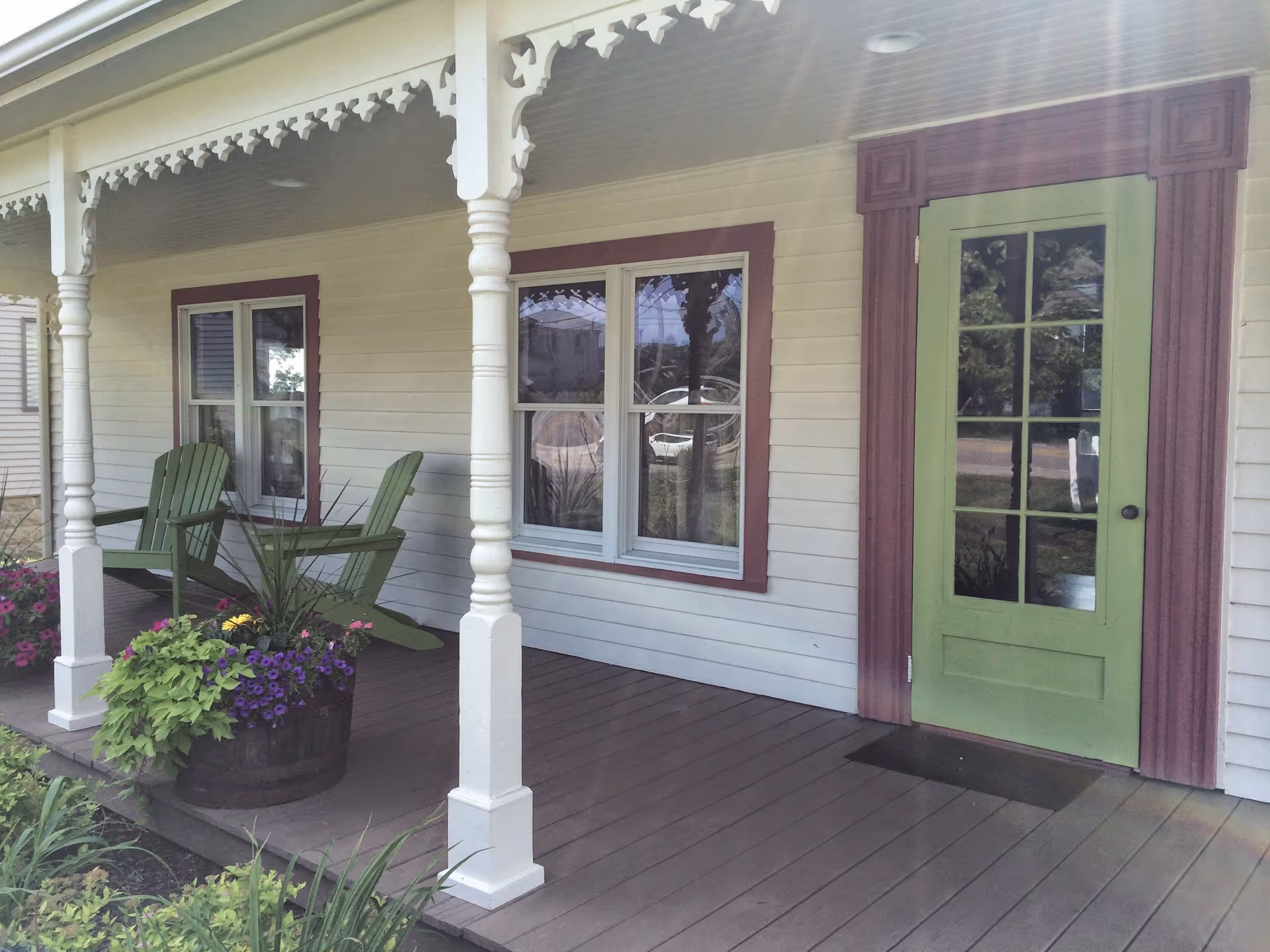 Front porch of a light-colored house with green door, windows, and two green chairs.