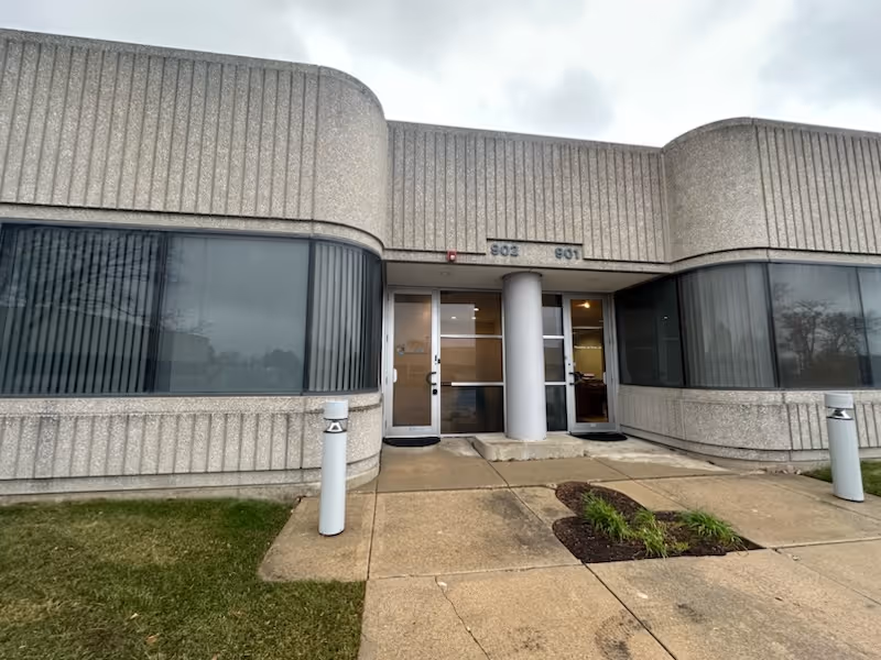Exterior view of a rounded concrete building entrance with glass doors and windows.