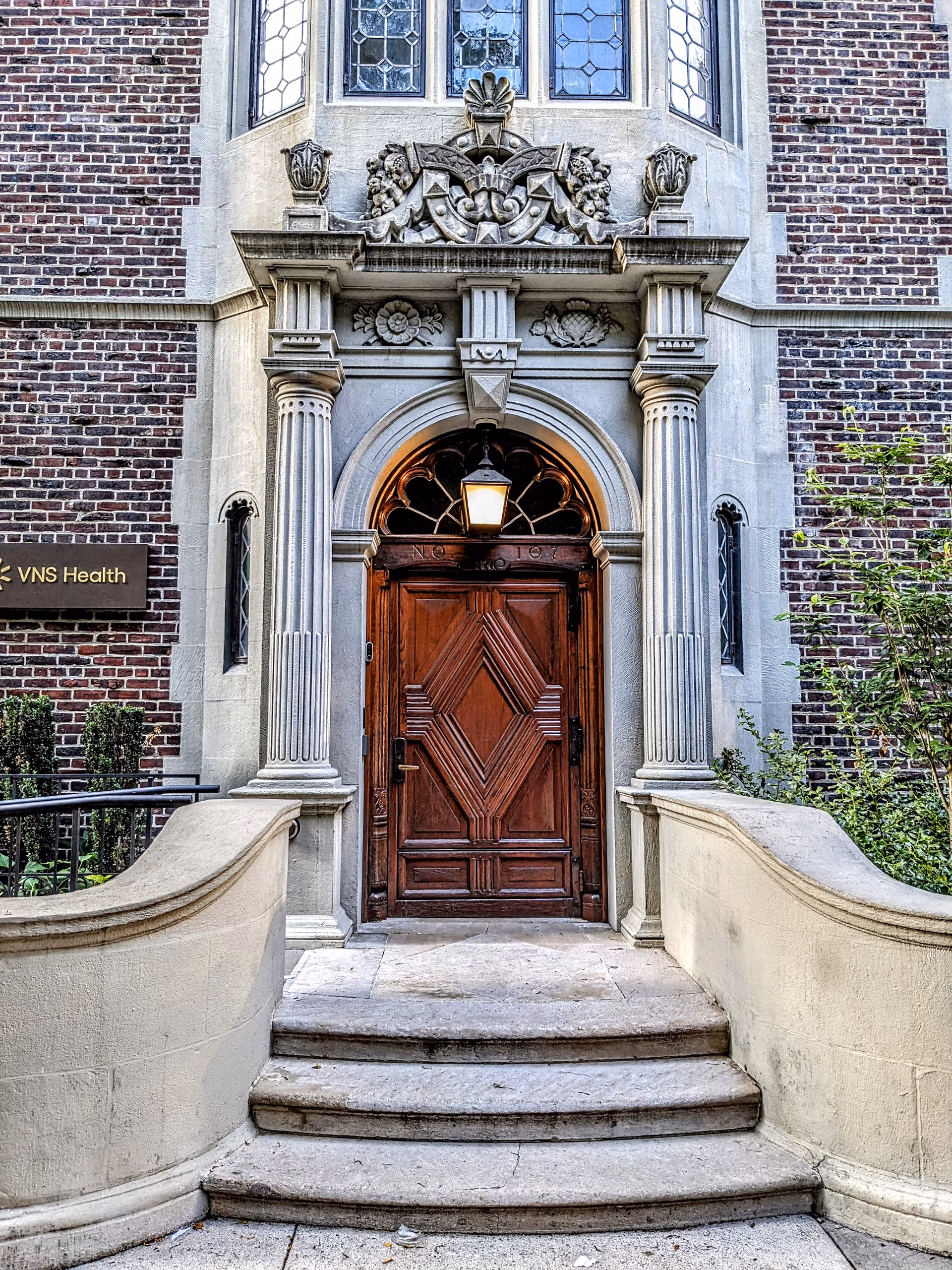 Stone-clad building entrance with decorative arch, wooden doors, and VNS Health sign.