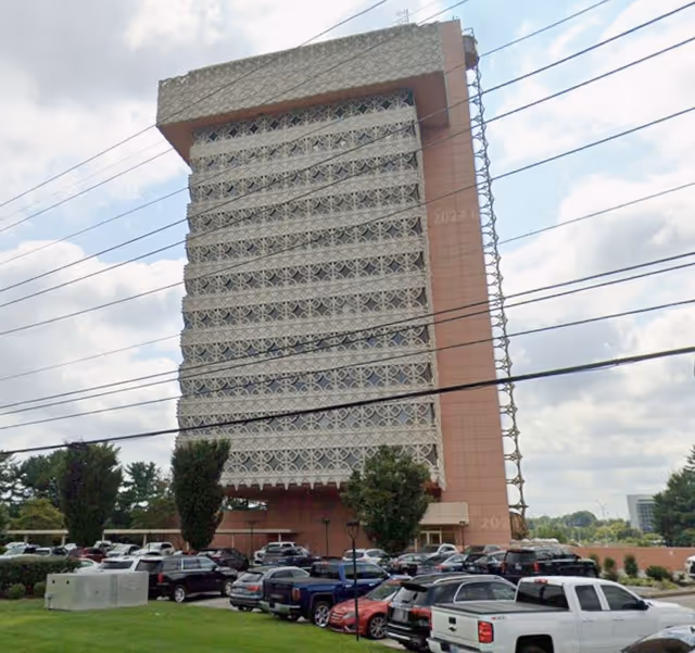 Exterior of a tall lattice-patterned building with a parking lot in front.