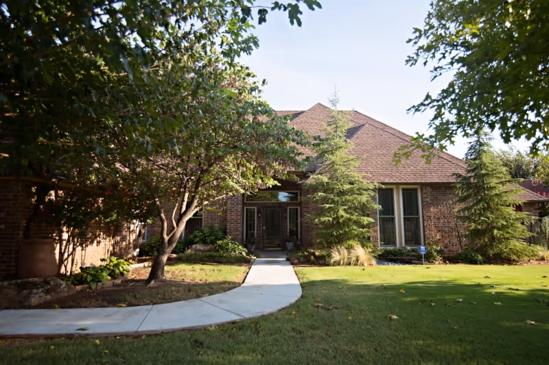 Exterior view of a brick senior living facility entrance with a curved walkway and trees.