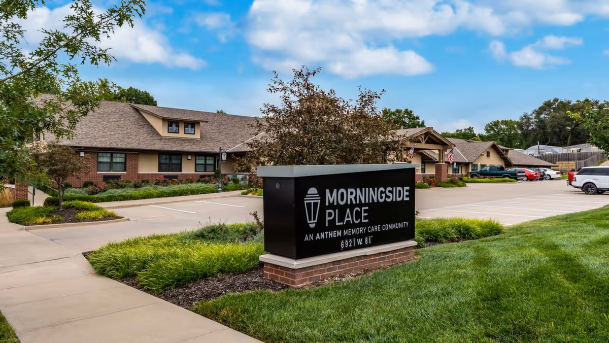 Entrance sign reading 'Morningside Place' in front of a one-story brick senior living building with landscaping and a parking lot.