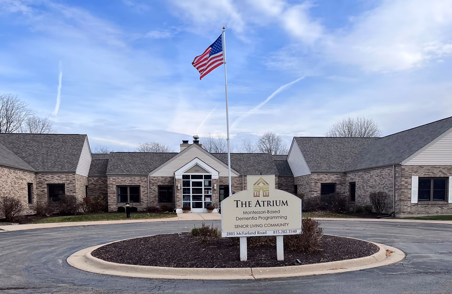 Brick senior living facility exterior with circular driveway, flagpole, and The Atrium sign in front.