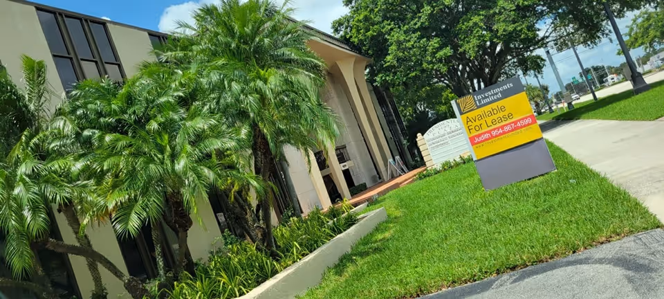 Exterior view of a senior living facility with palm trees and a lease sign.