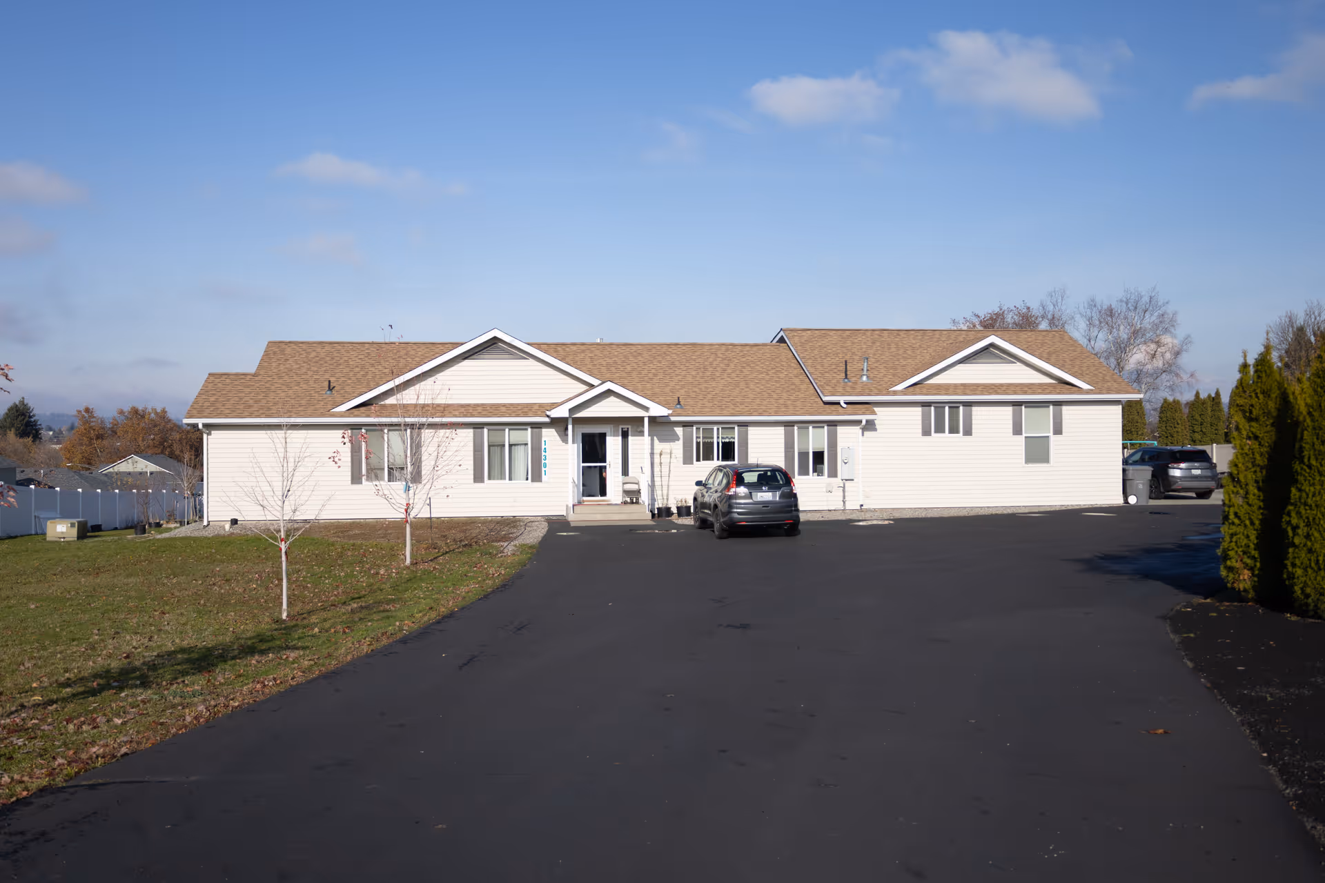 Single-story beige building with a long asphalt driveway and parked car.