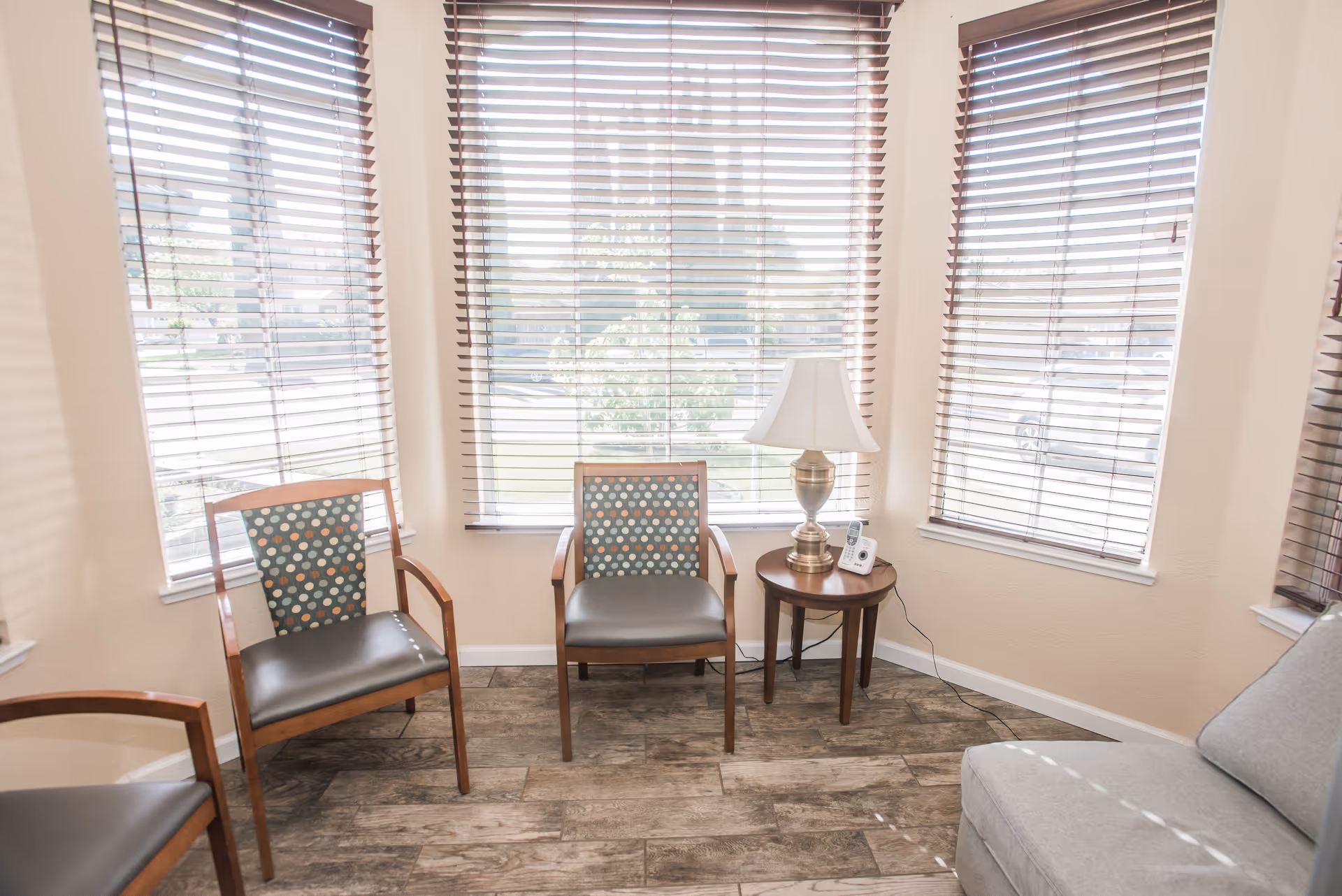 A cozy waiting lounge with three chairs, a sofa, and a side table by the windows.