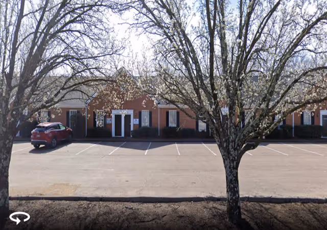 Front view of a brick senior care facility with a parking lot and trees.