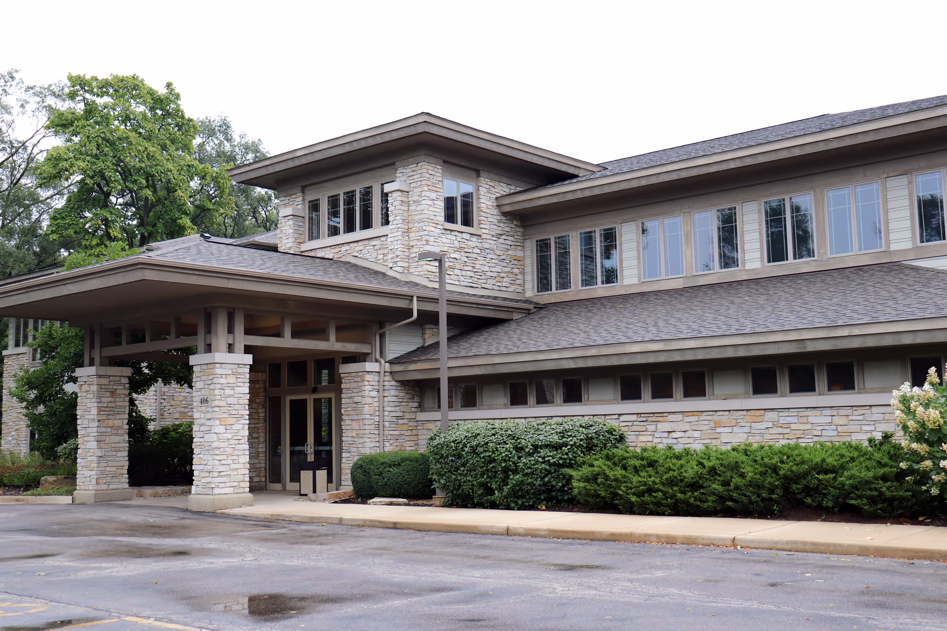 Stone-framed entrance of a modern senior living facility with landscaped bushes and windows.
