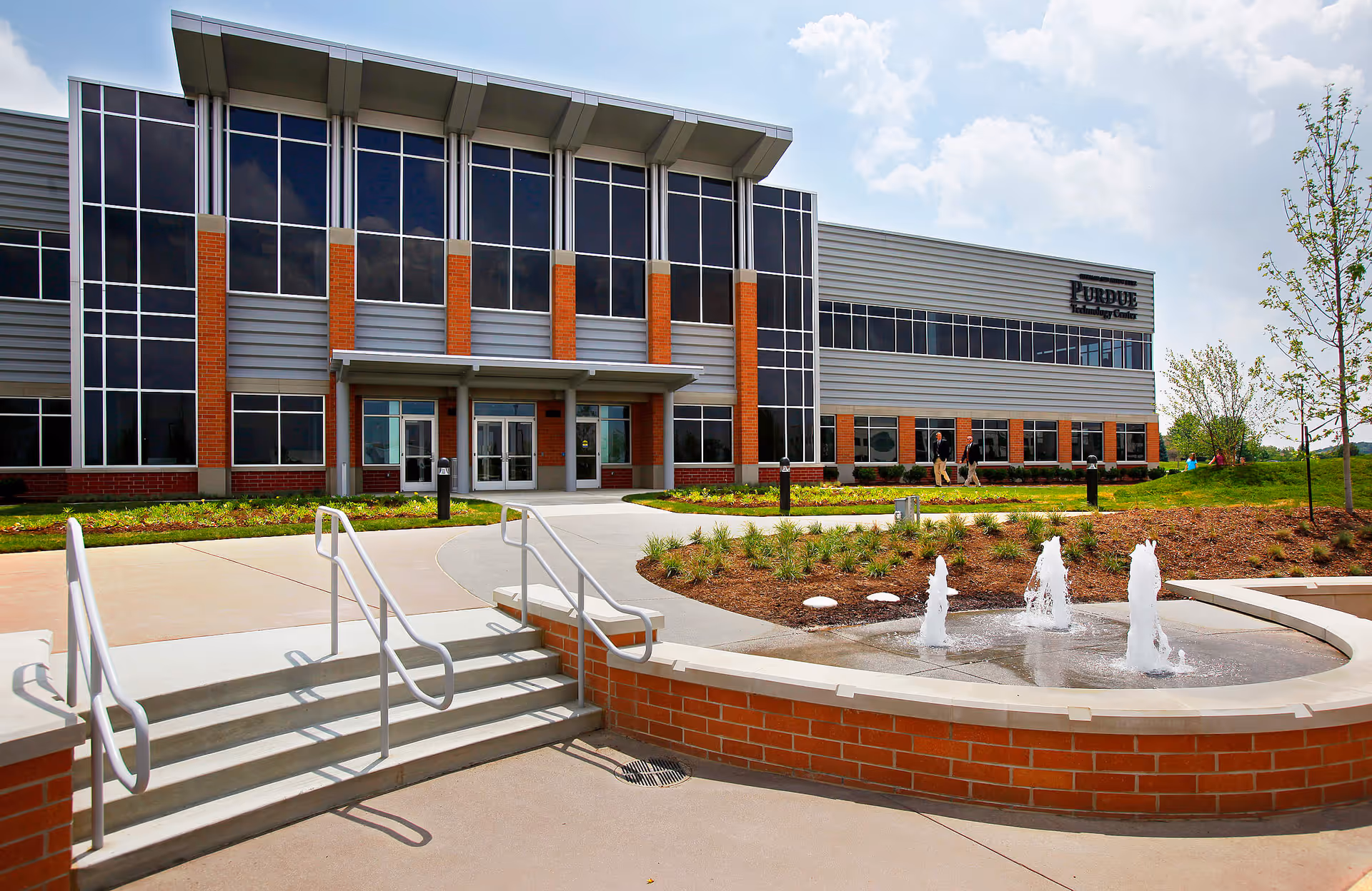 Modern senior living facility exterior with brick accents, glass facade, entrance, and circular fountain.