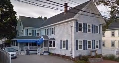 Two-story white senior home with blue shutters and a blue awning.