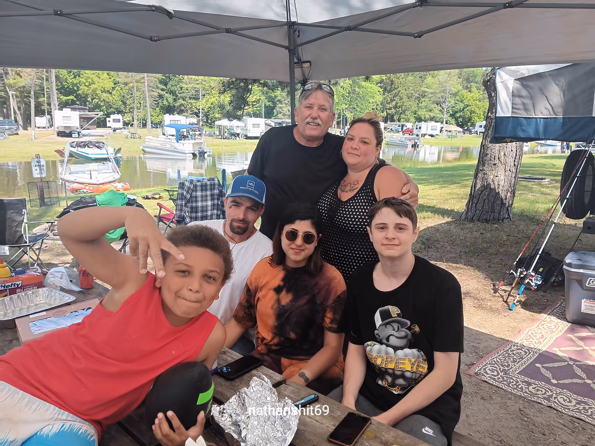 Group of diverse people under a canopy at a lakeside outdoor picnic.