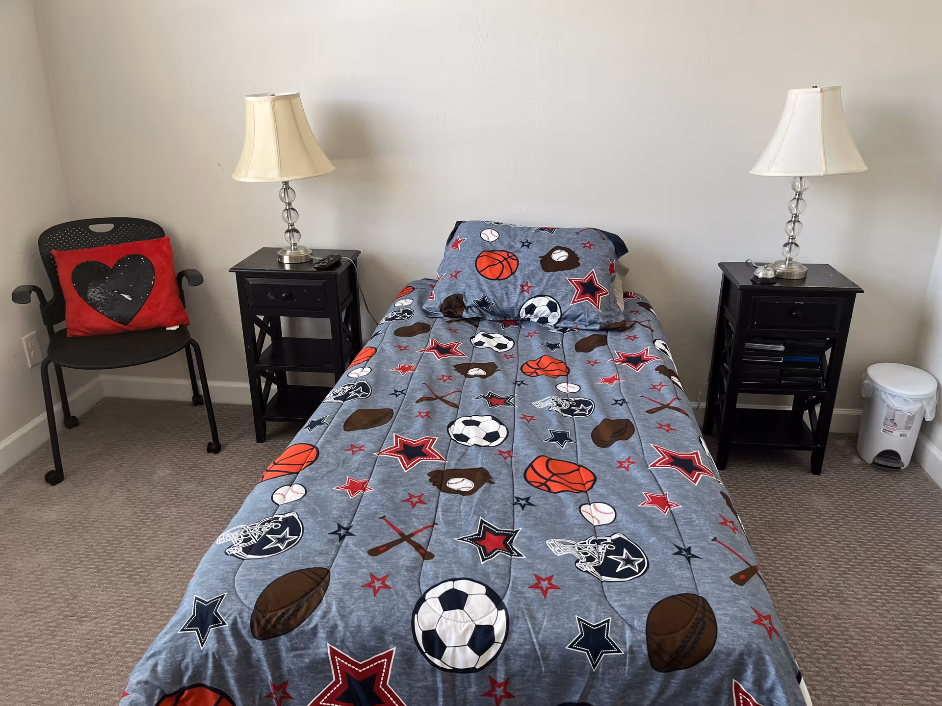 Twin bed with sports-themed bedding, two nightstands and lamps in a bedroom.