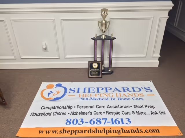 Trophy and award plaque beside a floor banner for Sheppard's Helping Hands in a hallway.