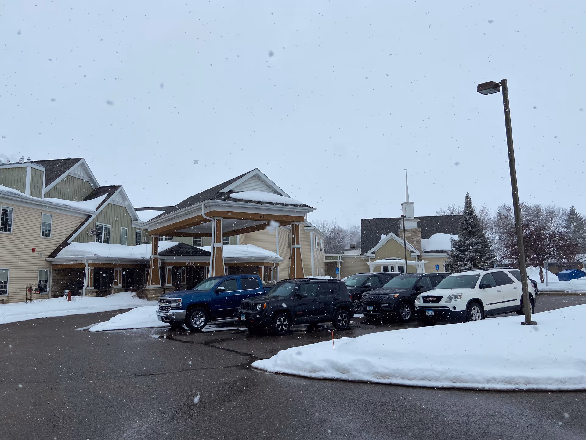 Snowy exterior of Park Terrace Assisted Living with a covered entrance and parked cars.