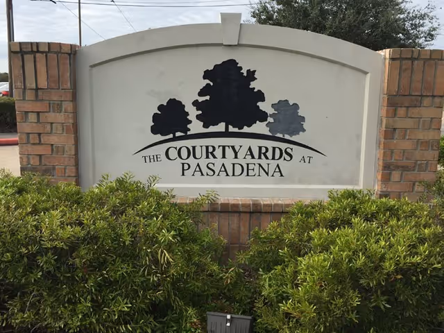 Stone sign reading 'The Courtyards at Pasadena' with brick pillars and shrubs.