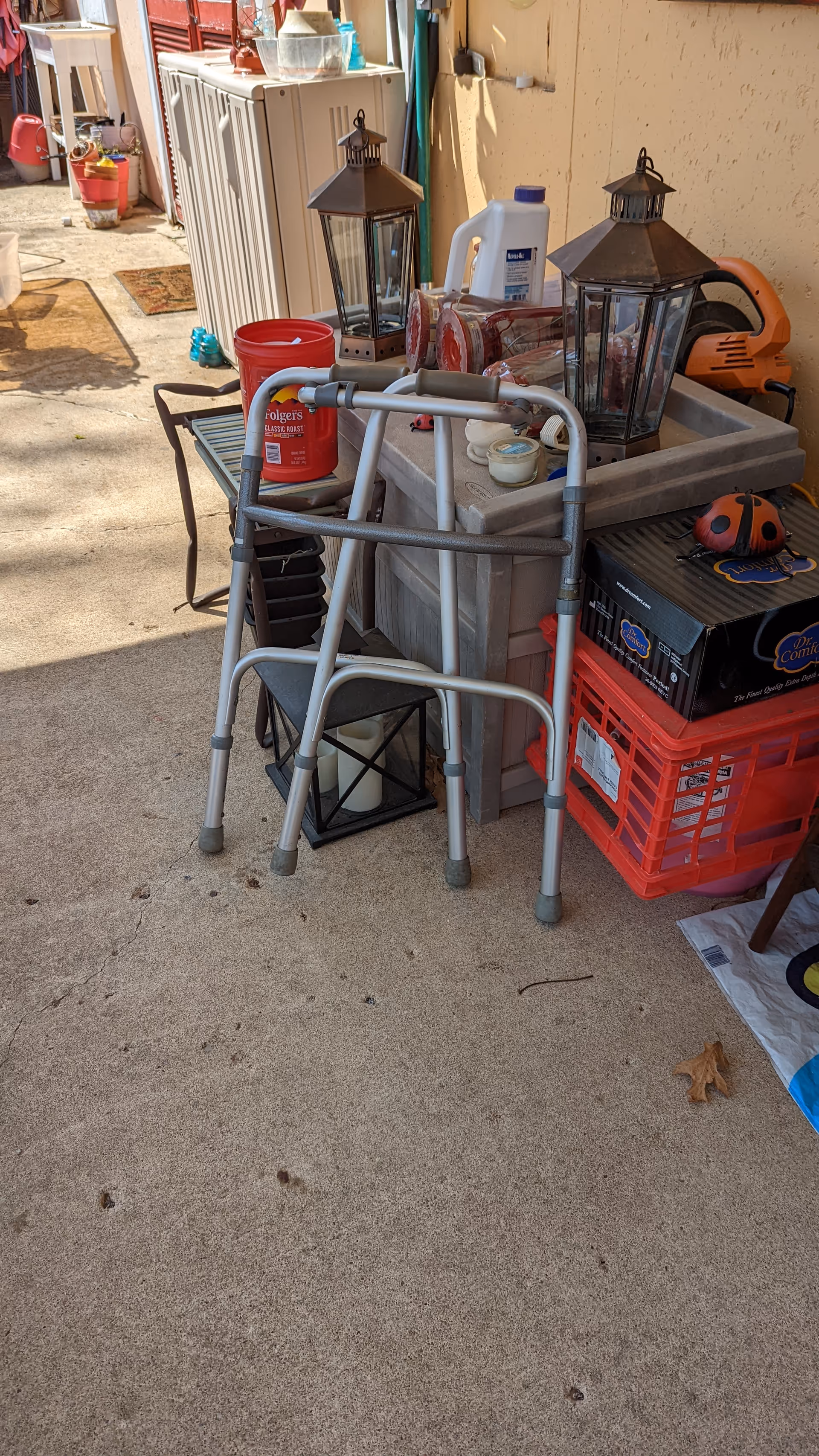 Outdoor storage area with a walker, lanterns, crates, and clutter on concrete.