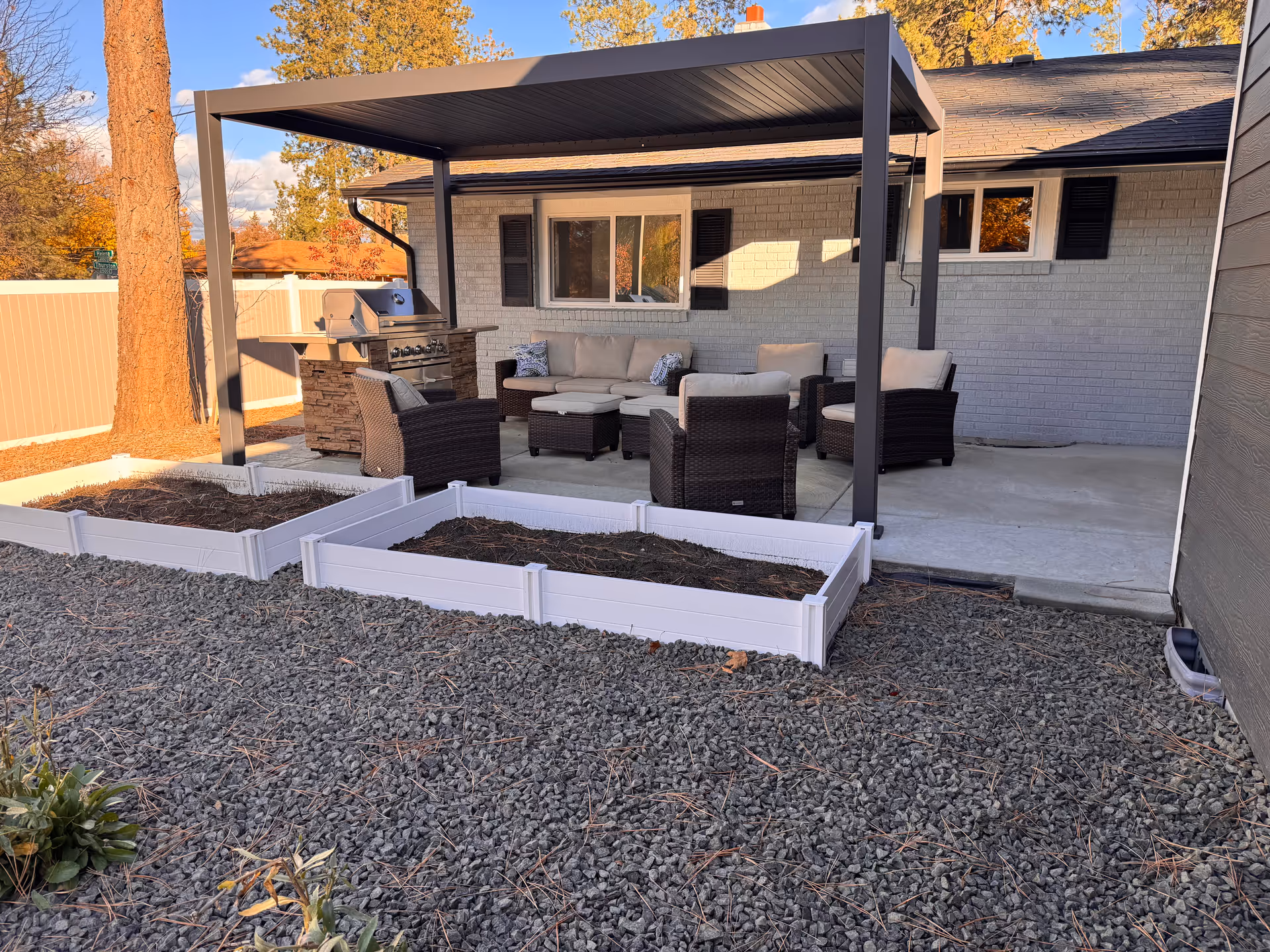 Outdoor patio with seating, a grill, raised garden beds, and a metal pergola by the house.