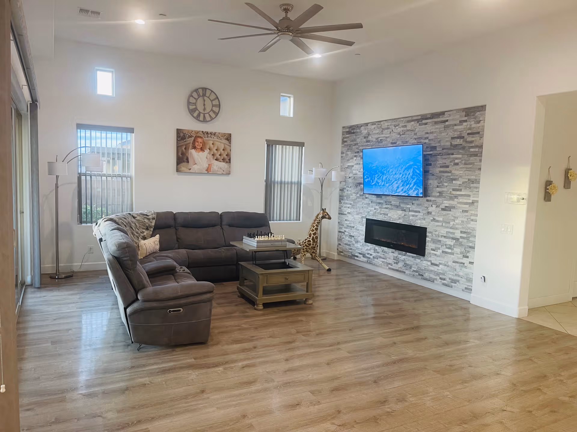 Spacious living room with gray sectional sofa, stone fireplace, TV, and ceiling fan.