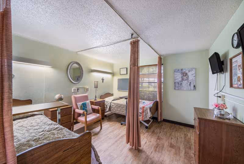 Shared senior living bedroom with privacy curtains, multiple beds, and a dresser.