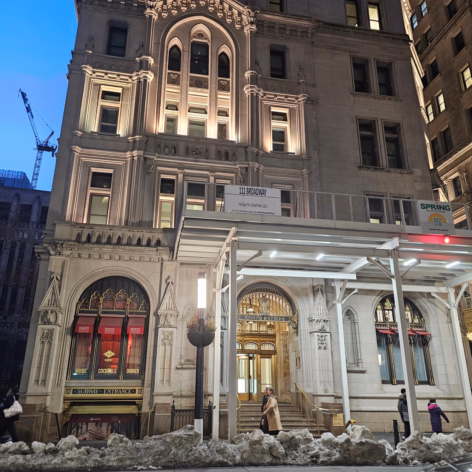Night exterior of an ornate building with a subway entrance and snowy sidewalk.
