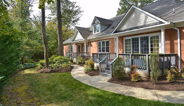 Exterior of a brick senior living facility with porches and landscaped walkway.