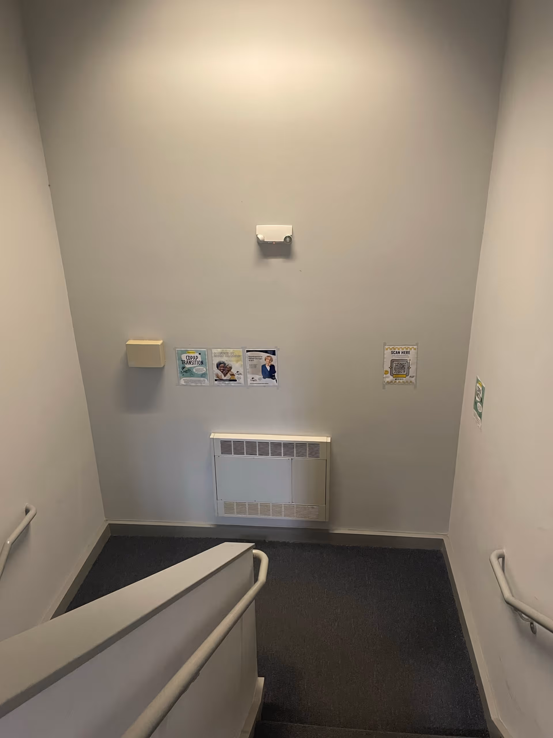 Indoor stairwell in a senior living facility with handrails and wall posters.