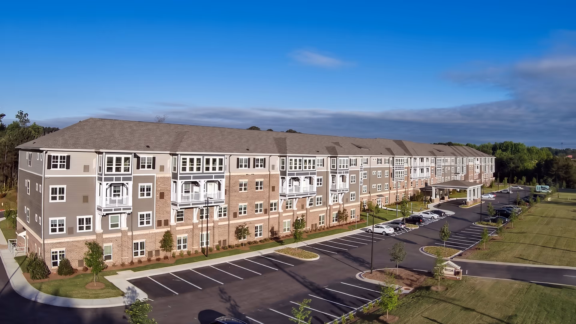 A long beige senior living building with stone accents, parking lot, and green lawn.