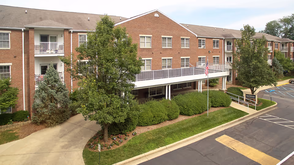 Brick senior living facility exterior with landscaped entrance and flagpole along a driveway.