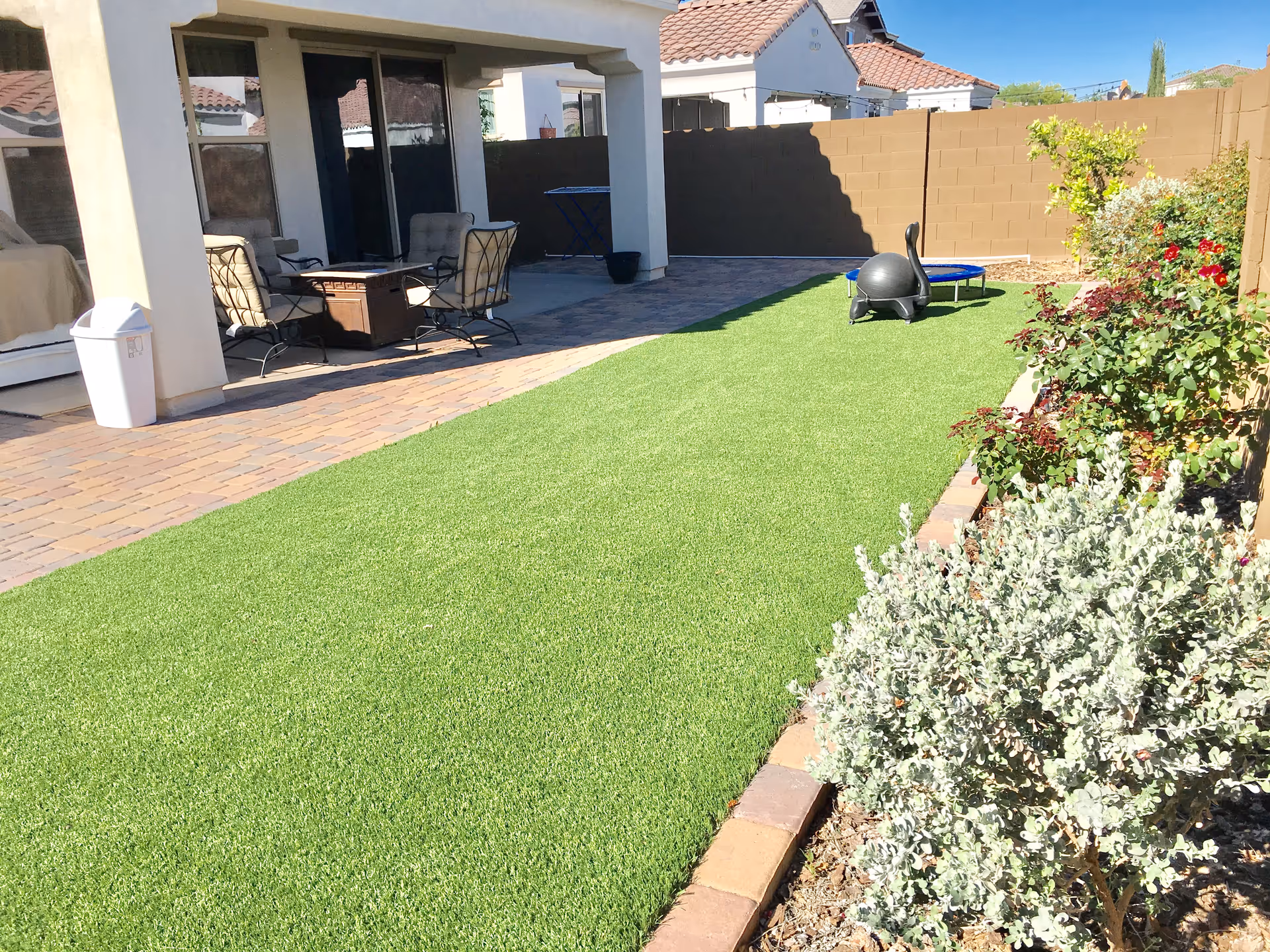 Outdoor patio area with seating, artificial lawn, and landscaped shrubs.