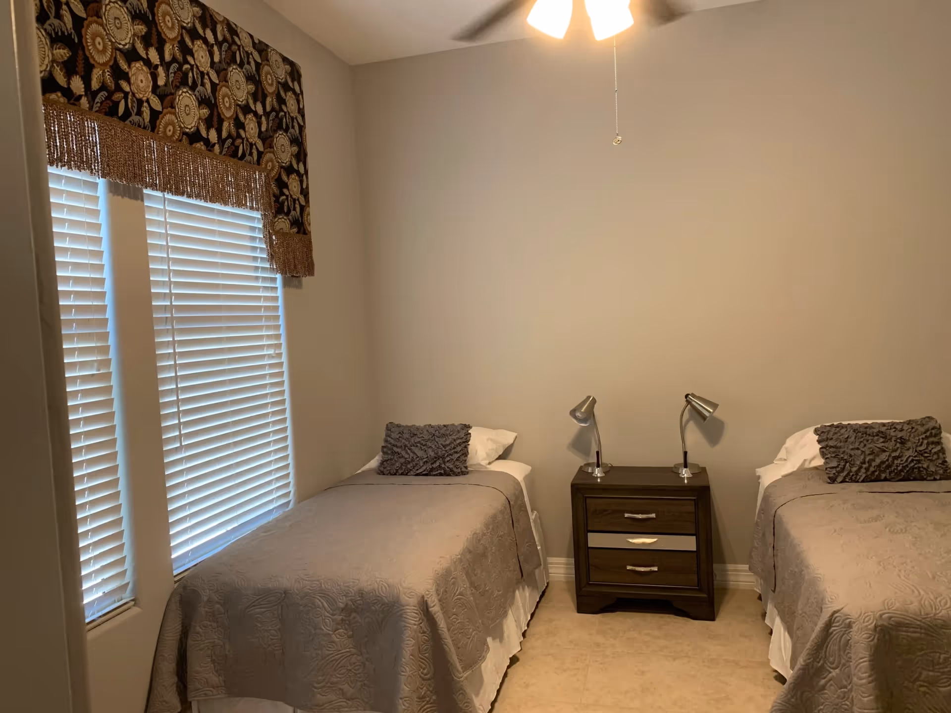 Two twin beds with matching gray quilts flank a wooden nightstand in a cozy bedroom.