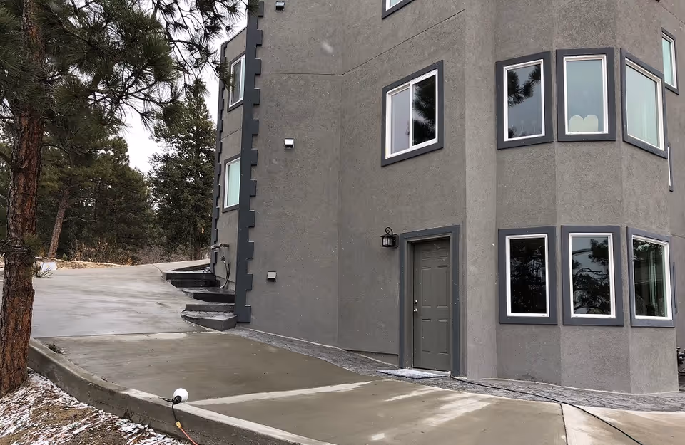 Gray, multi-story building exterior with several windows, a door, and surrounding trees.