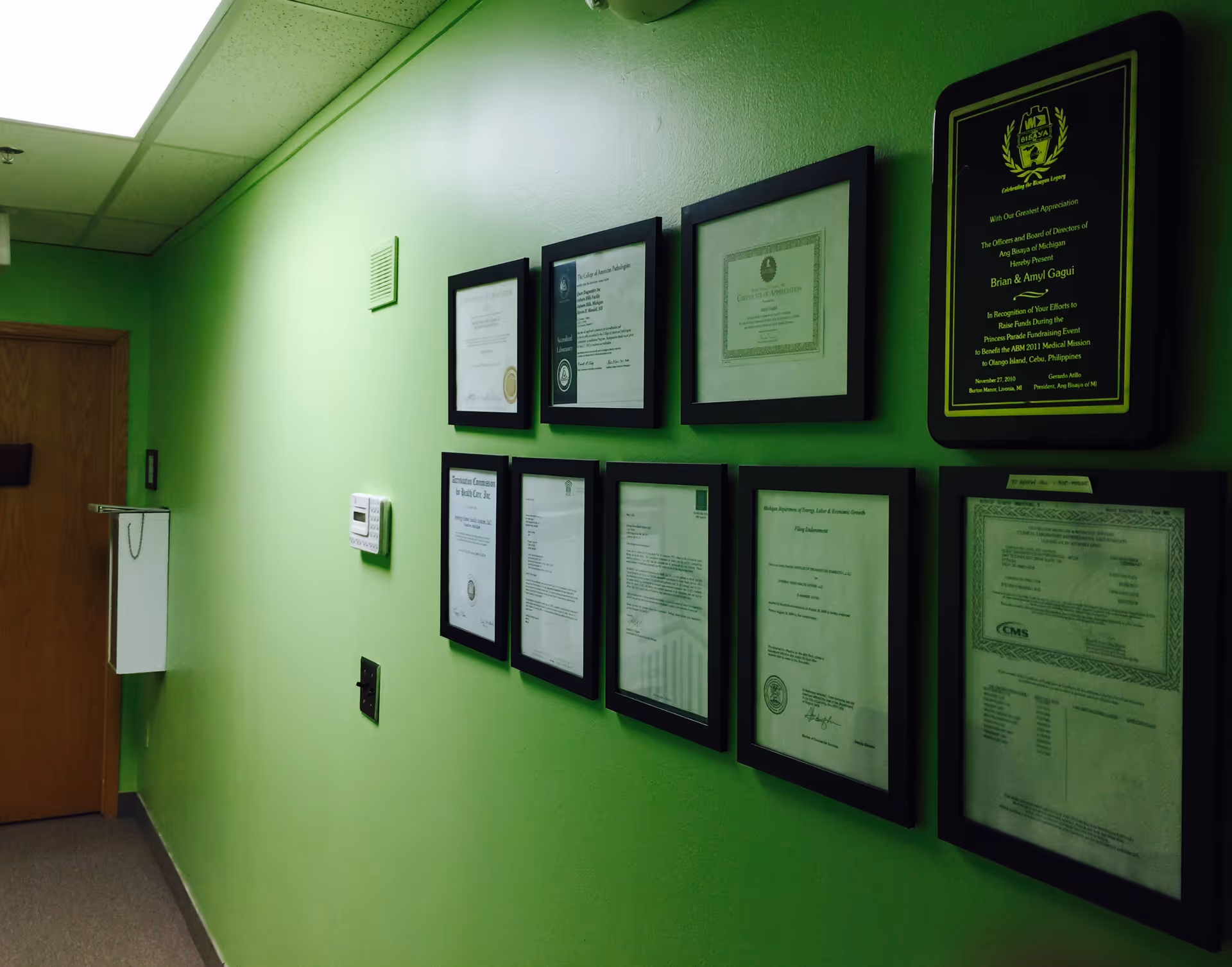 Bright lime-green hallway with multiple framed certificates displayed along the wall.