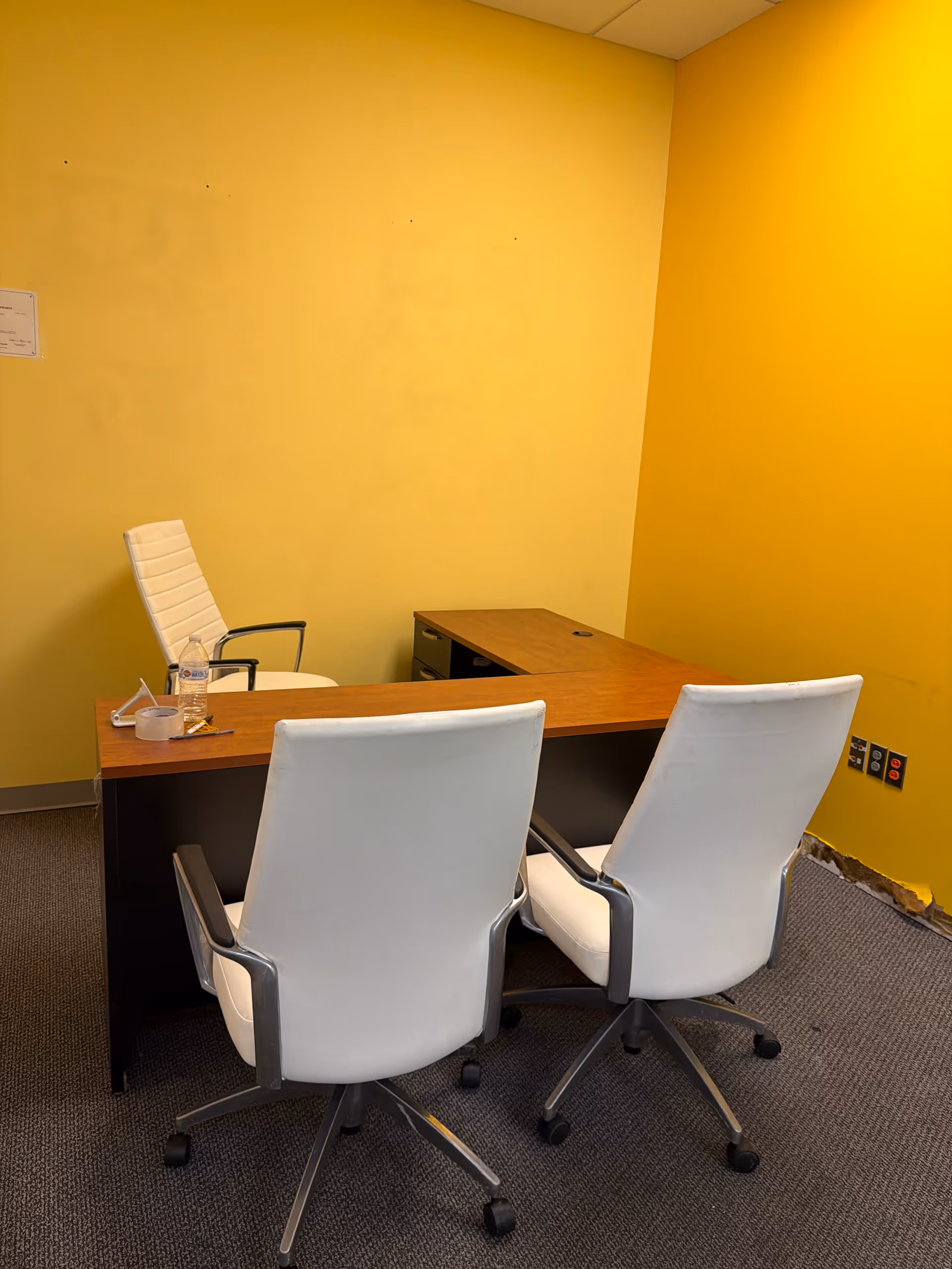 Yellow-walled office with a wooden desk and white chairs.