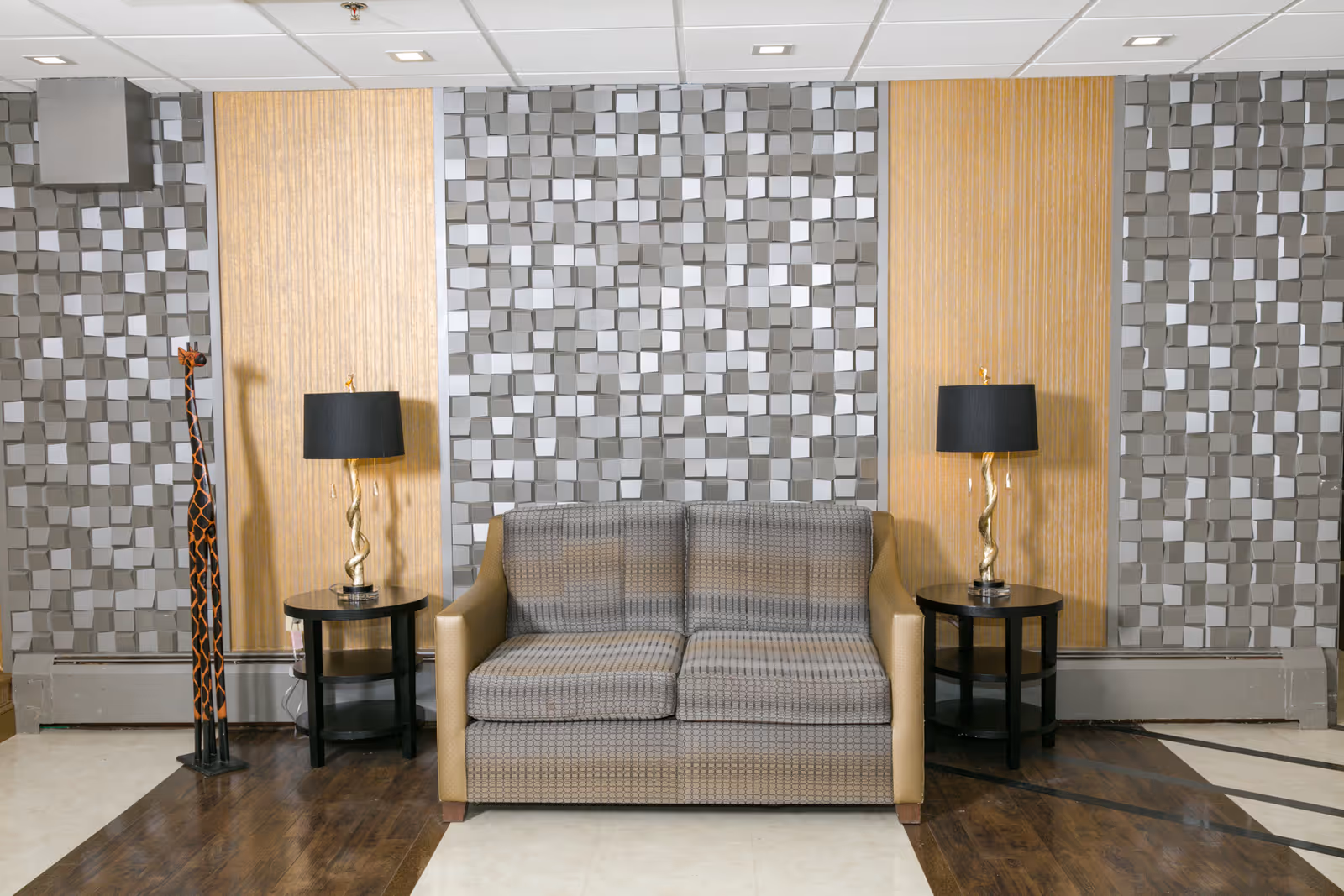 A modern lobby seating area with a gray sofa, two side tables, and lamps.