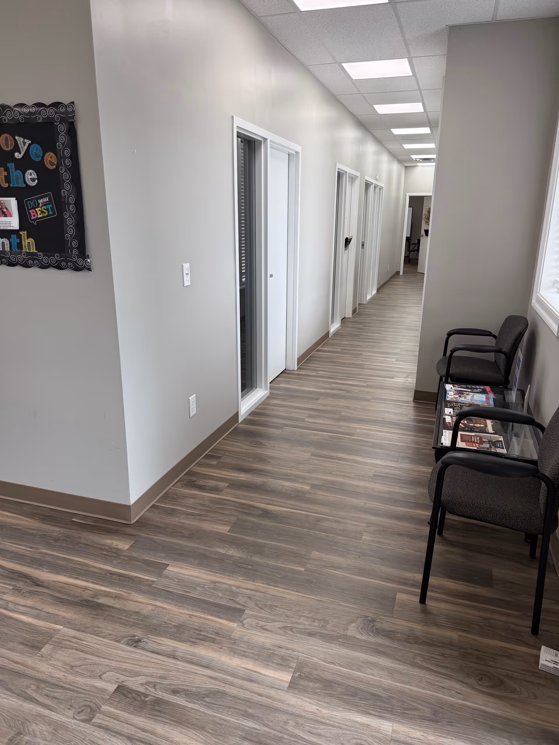 A long, well-lit hallway in a senior care facility with doors and waiting chairs.