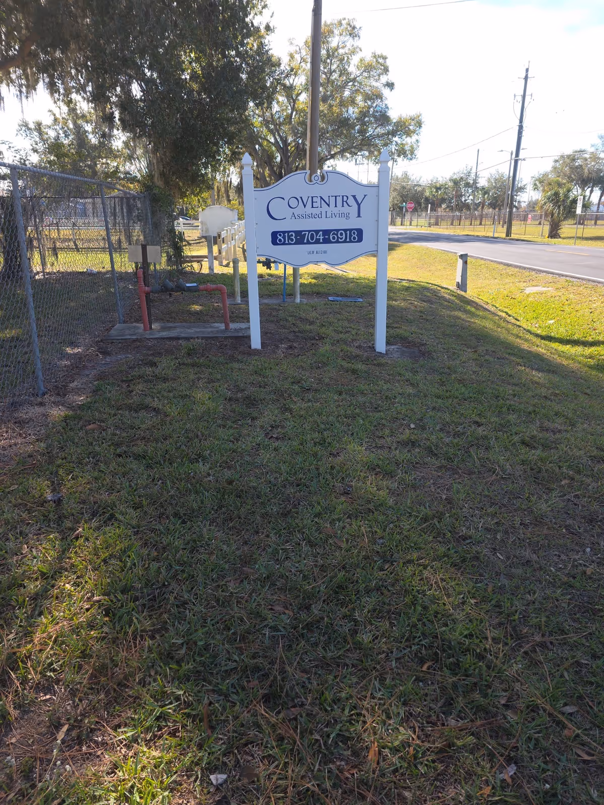 Outdoor grassy area with Coventry Assisted Living sign beside a road