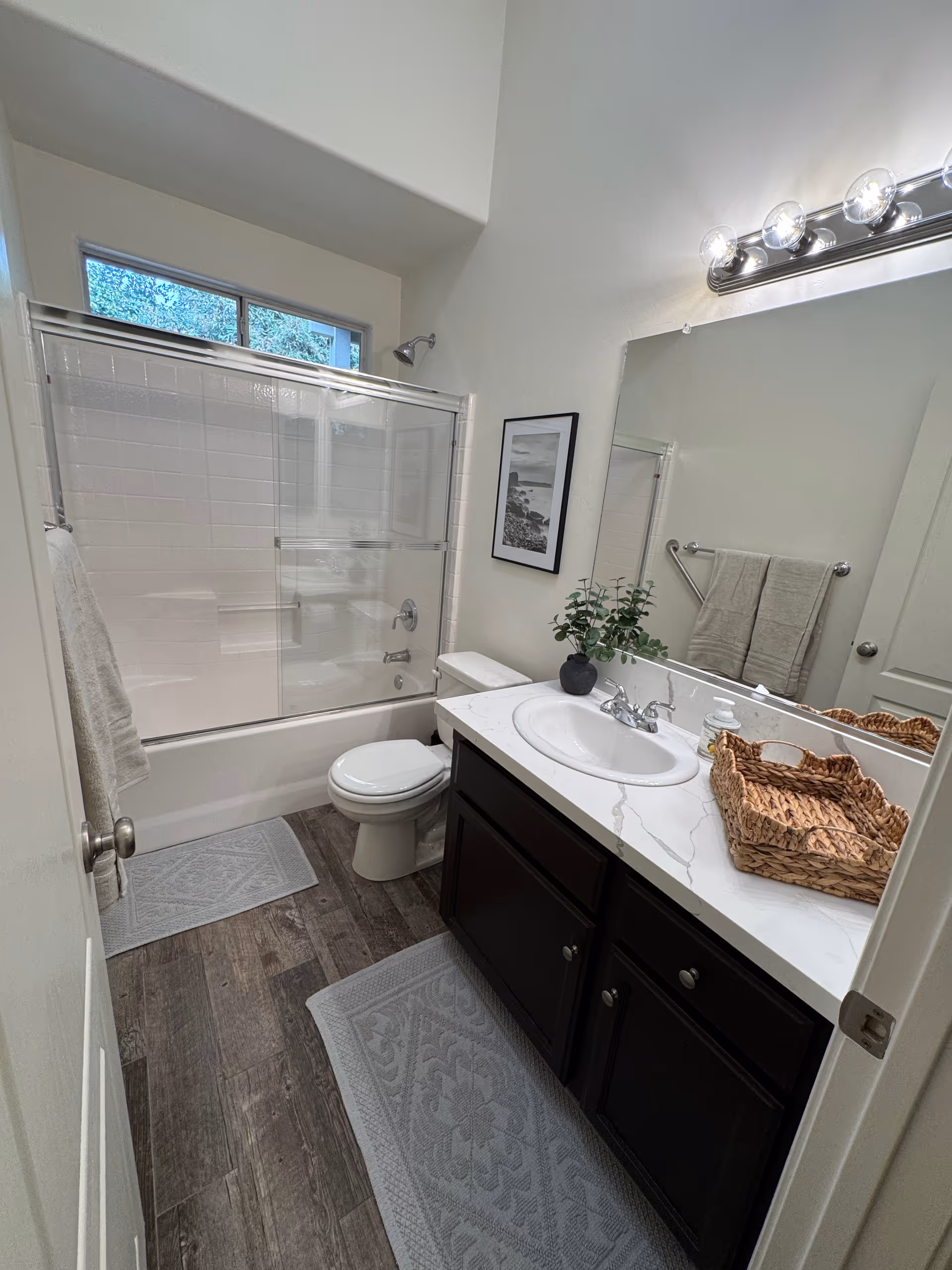 Bright bathroom with a bathtub, vanity, mirror, towels, and plant decor.