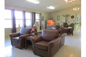 A spacious senior living lounge with brown leather seating and bright windows.