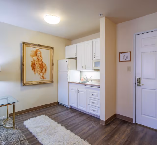 Compact white kitchen with cabinets, fridge, sink, and doorway in a cozy apartment.