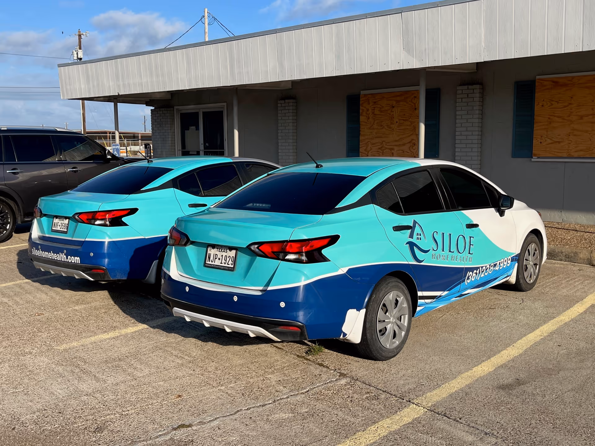 Two teal Siloe Home Health branded cars parked outside a gray building.