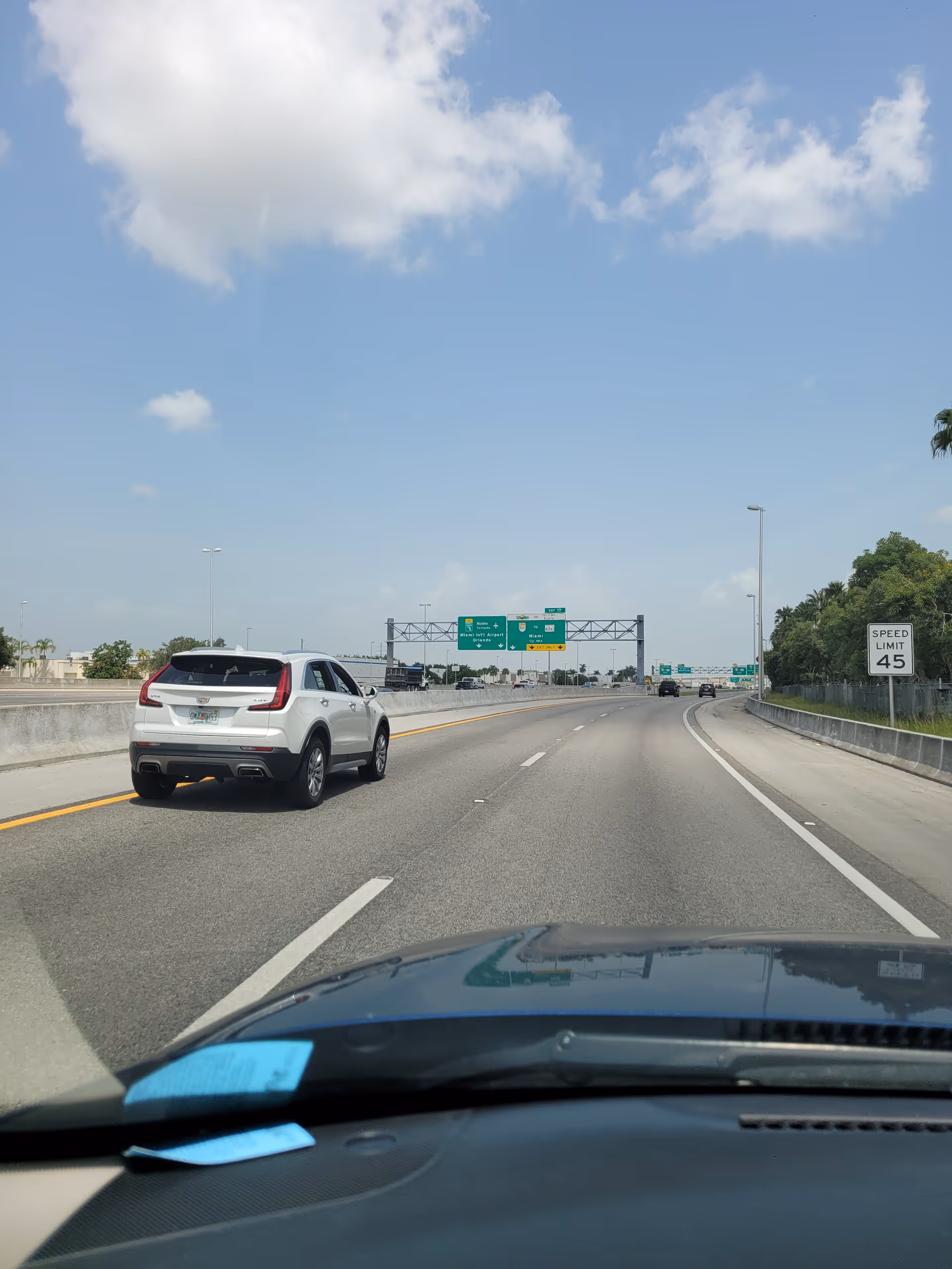 View from a car on a sunny highway with cars and overhead green road signs.